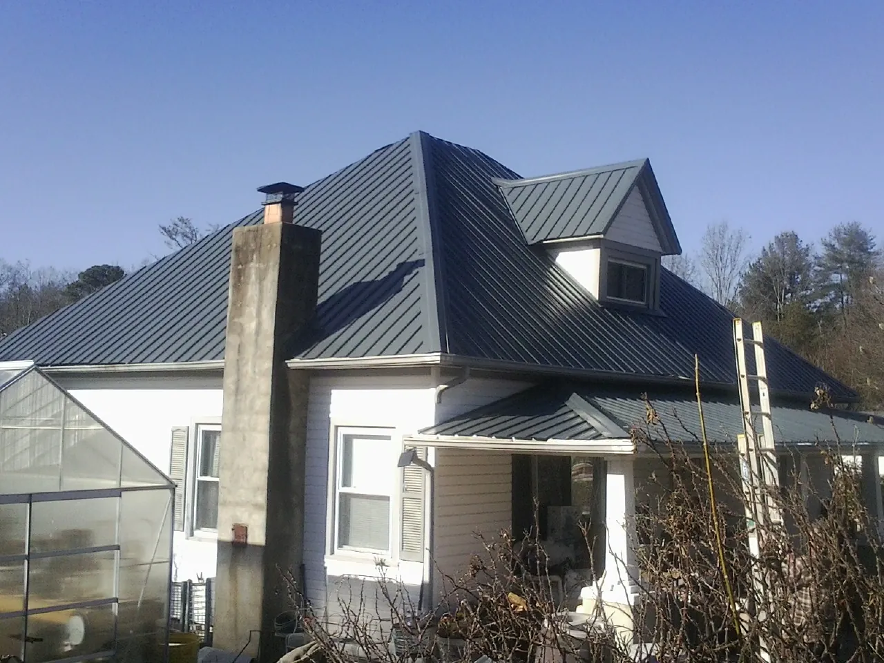 Dark blue standing seam metal roof on a white farmhouse with dormer — Slate & Tile Roof Repair by Roofing Brothers in Windermere