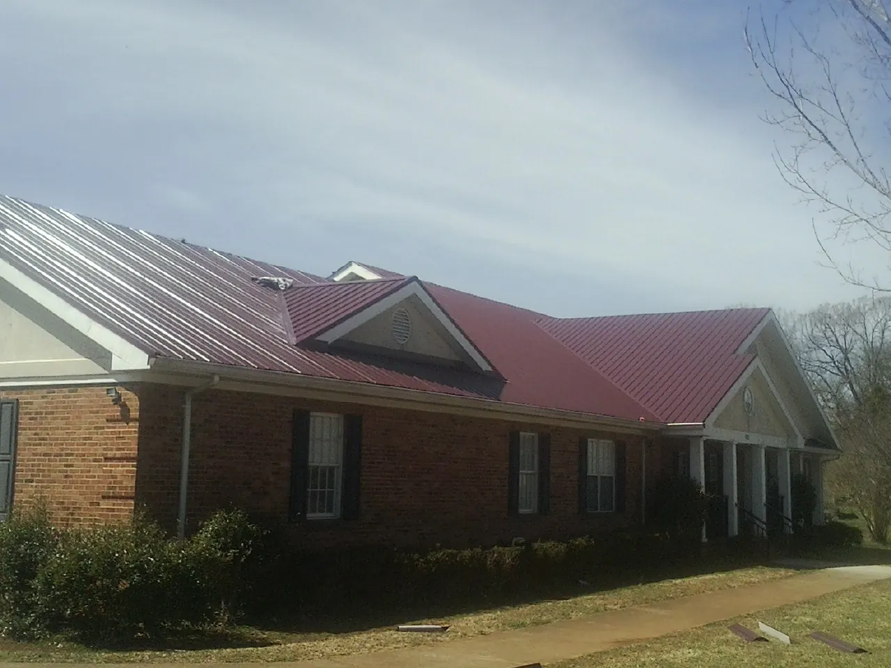 Red metal roof with gabled entries on a long brick building, from a Hail Damage Roof Repair job in Windermere