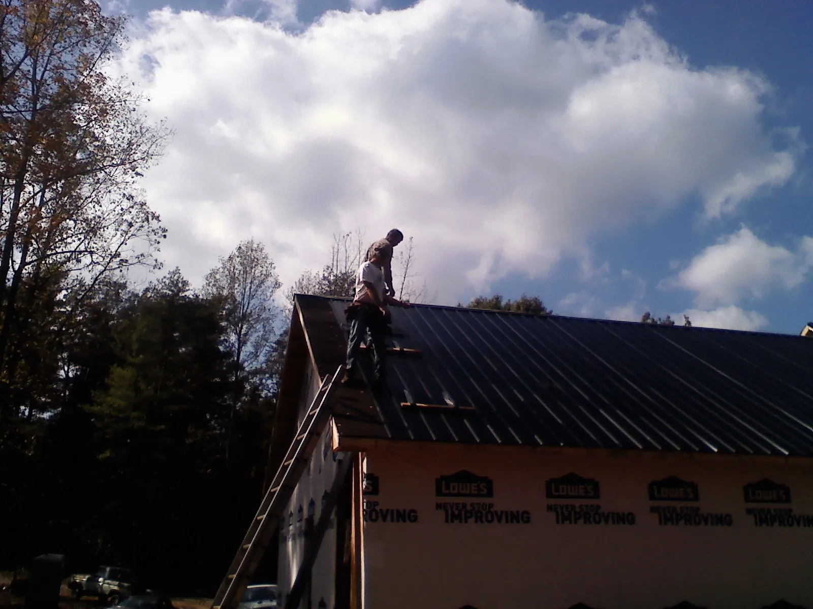 Roofer fastening dark metal panels high against a cloudy sky, from a Roof Inspection job in Windermere